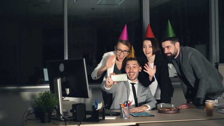 Kollegen mit Partyhüten machen auf einer Feier im Büro ein Selfie